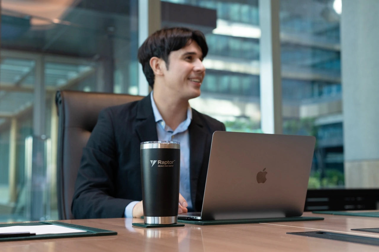 Man sitting at a desk with a laptop and a branded tumbler in an office setting