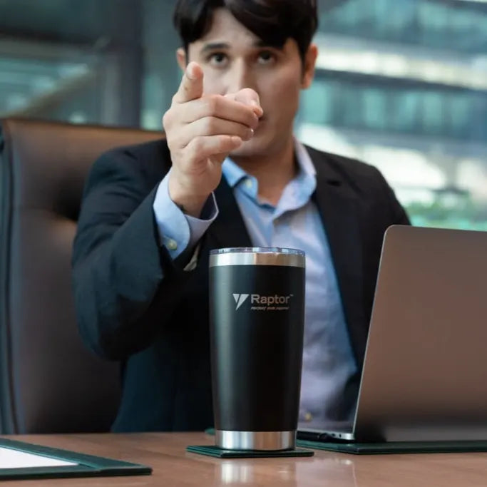 Man in a suit sitting at a desk with a laptop and Raptor tumbler.